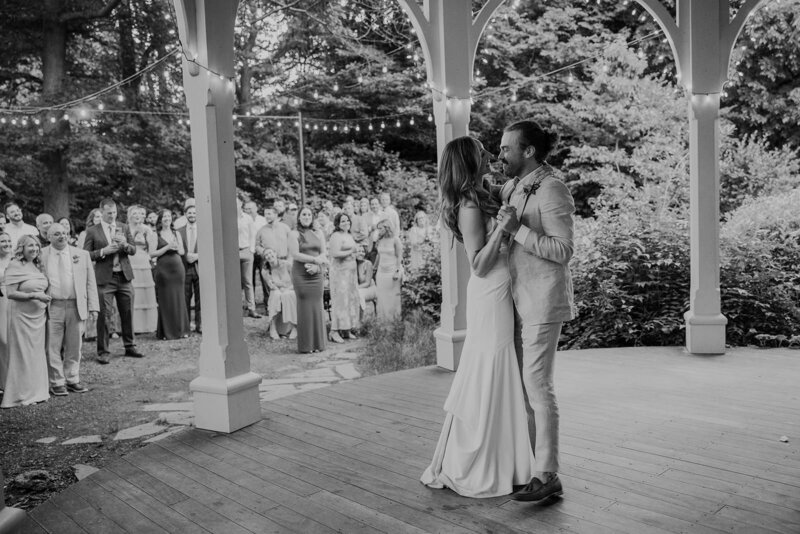 a couple shares the first dance of their wedding day on the patio while their families watch