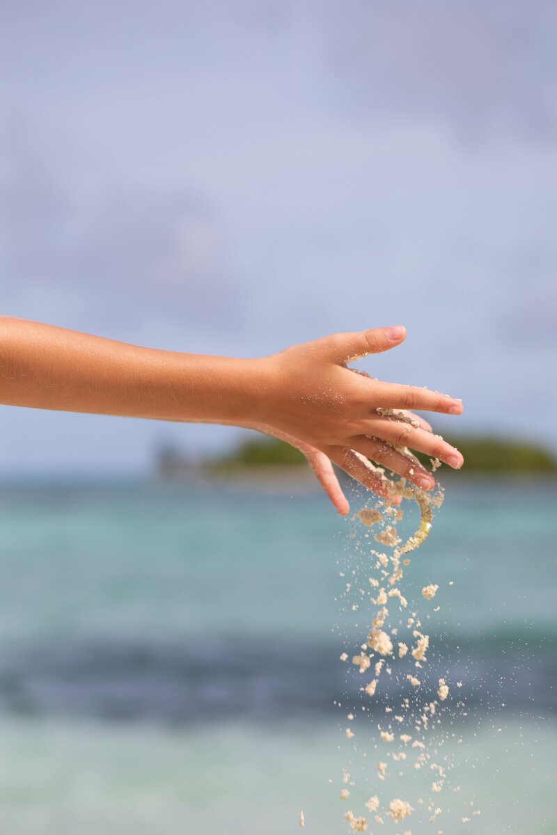 A child’s hand letting sand fall at the beach, symbolizing sensory play and the calming, child-centered approach of Pacific Kids Occupational Therapy in Orange County.
