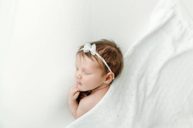 baby girl with headband is sleeping under a white blanket during her Newborn session in Atlanta