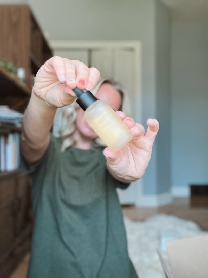 Kesley Hansen wearing a green t-shirt holding a bottle of the Dermatology Serum EX in front of her face