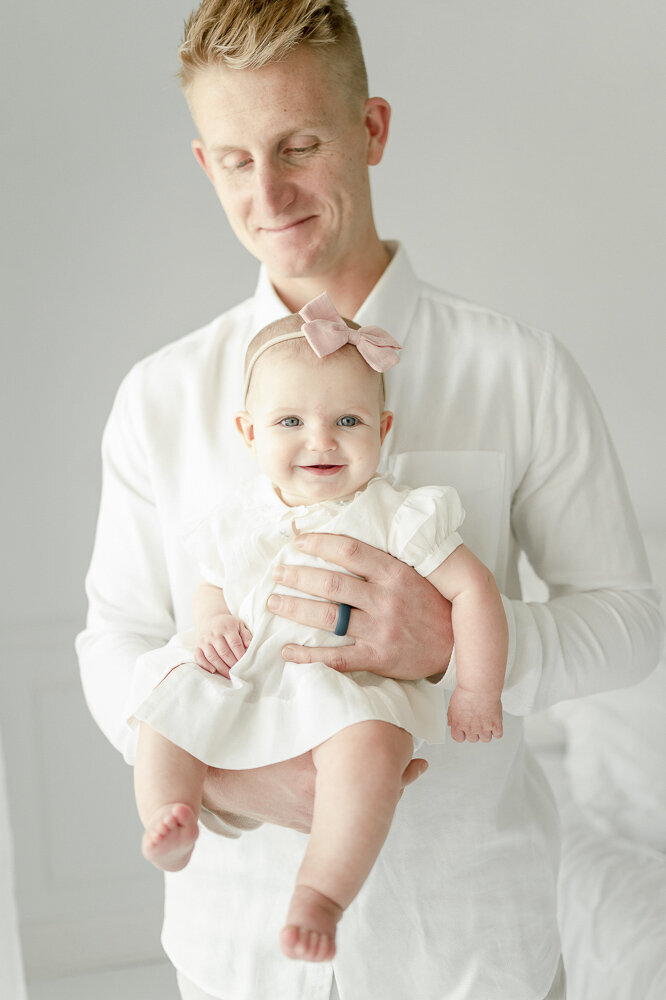 A dad holds his 6 month old baby wearing a pink bow