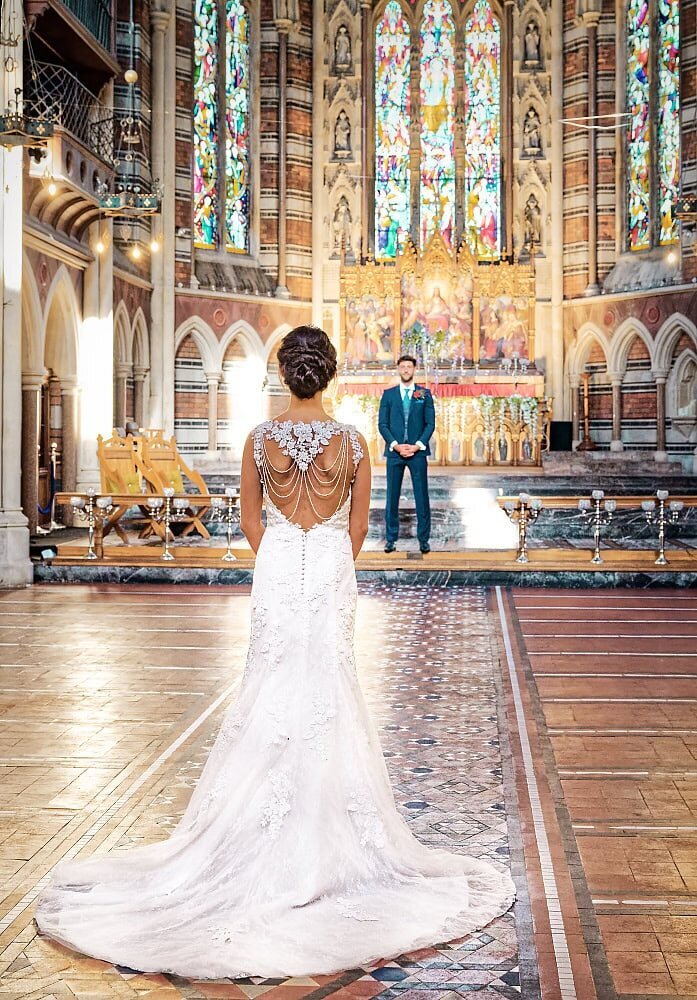 view from behind the bride, looking at her groom in a chapel surrounded by stained glass windows