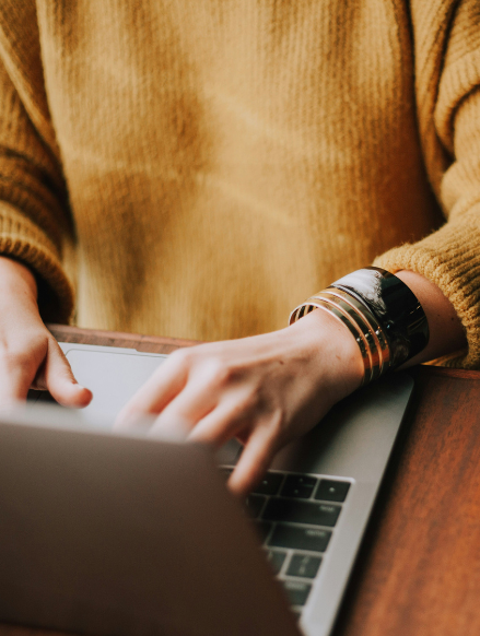Close-up of hands typing on a laptop, with a cozy sweater and statement bracelet, reflecting a personal and approachable way to connect for consulting support.