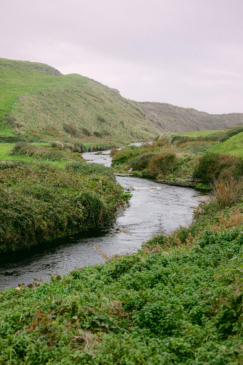 Photo of a river in Ireland flowing through a green field close to the Cliffs of Moher