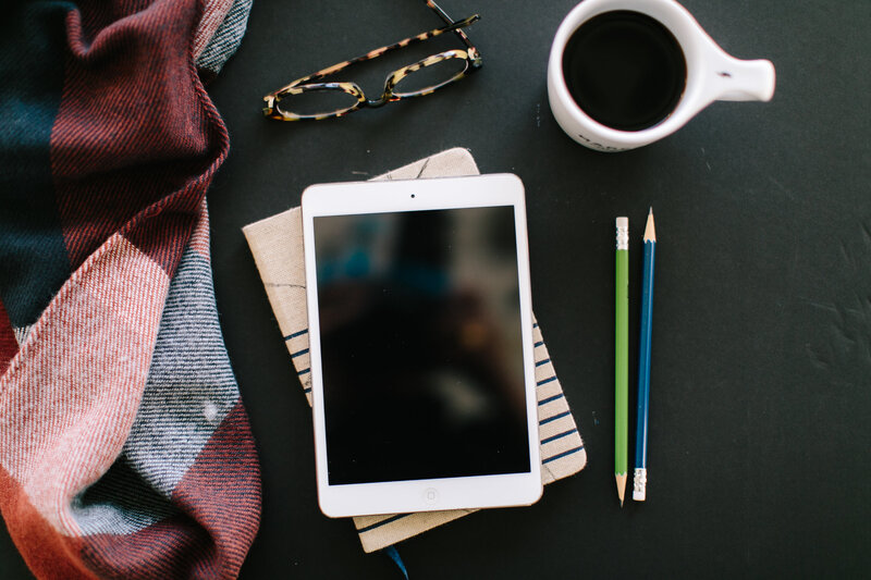 white ipad with black coffee and glasses with a notebook and pencils on table 