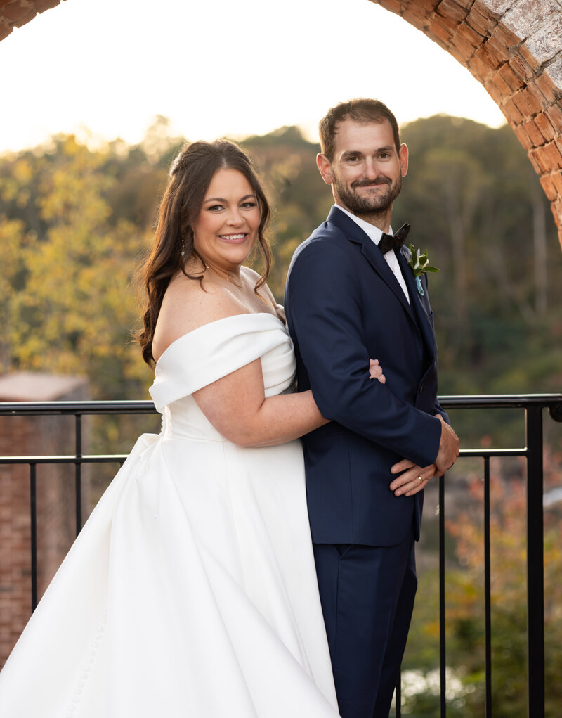 bride wearing lace spaghetti strap dress and groom wearing gray suit smiling at camera