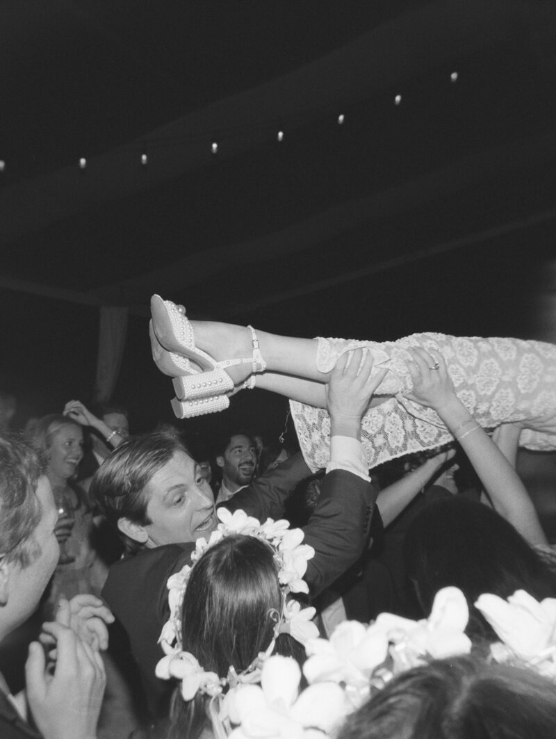 Black and white film photo of bride's legs held in the air by reception guests