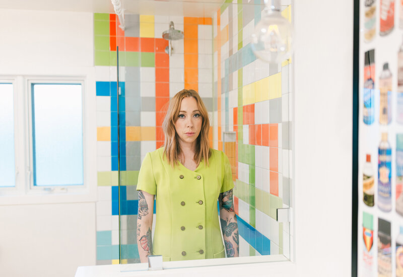 Editorial branding portrait of a creative entrepreneur in a bold green outfit, photographed in a colorful modern studio space with graphic tile design. Branding photography of interior designer.