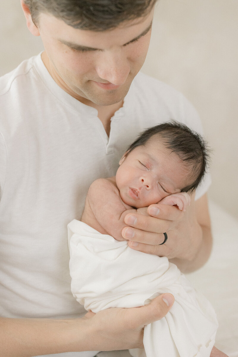 A dad holding his newborn baby facing outwards in all white studio by New Jersey baby photographer