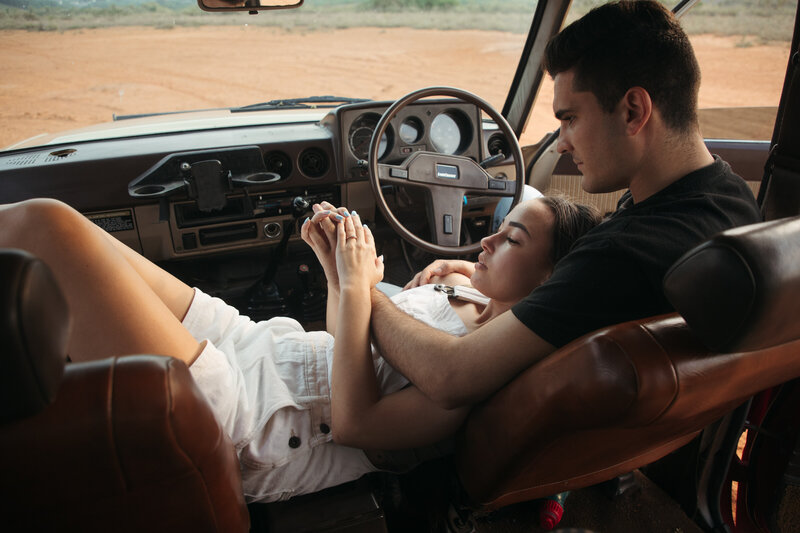 A couple share a moment in a retro ute , they are tenderly playing with each other's hands