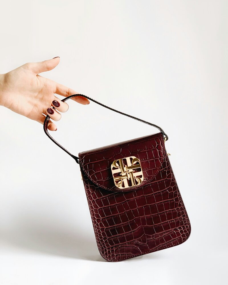 Hand with burgundy nails holding the handle of a burgundy purse on a white background