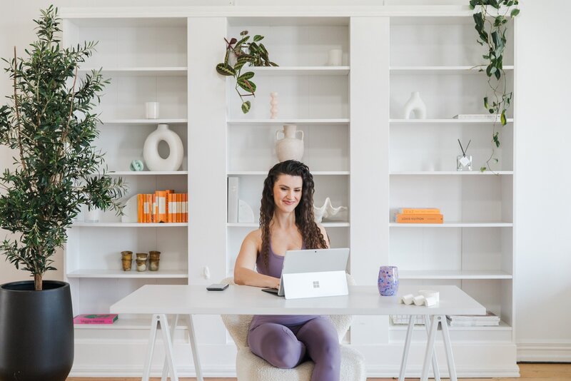 Hailey Ann Co Bookkeeper and Somatic Money Coach for Female Entrepreneurs sitting at desk, working and smiling at a laptop
