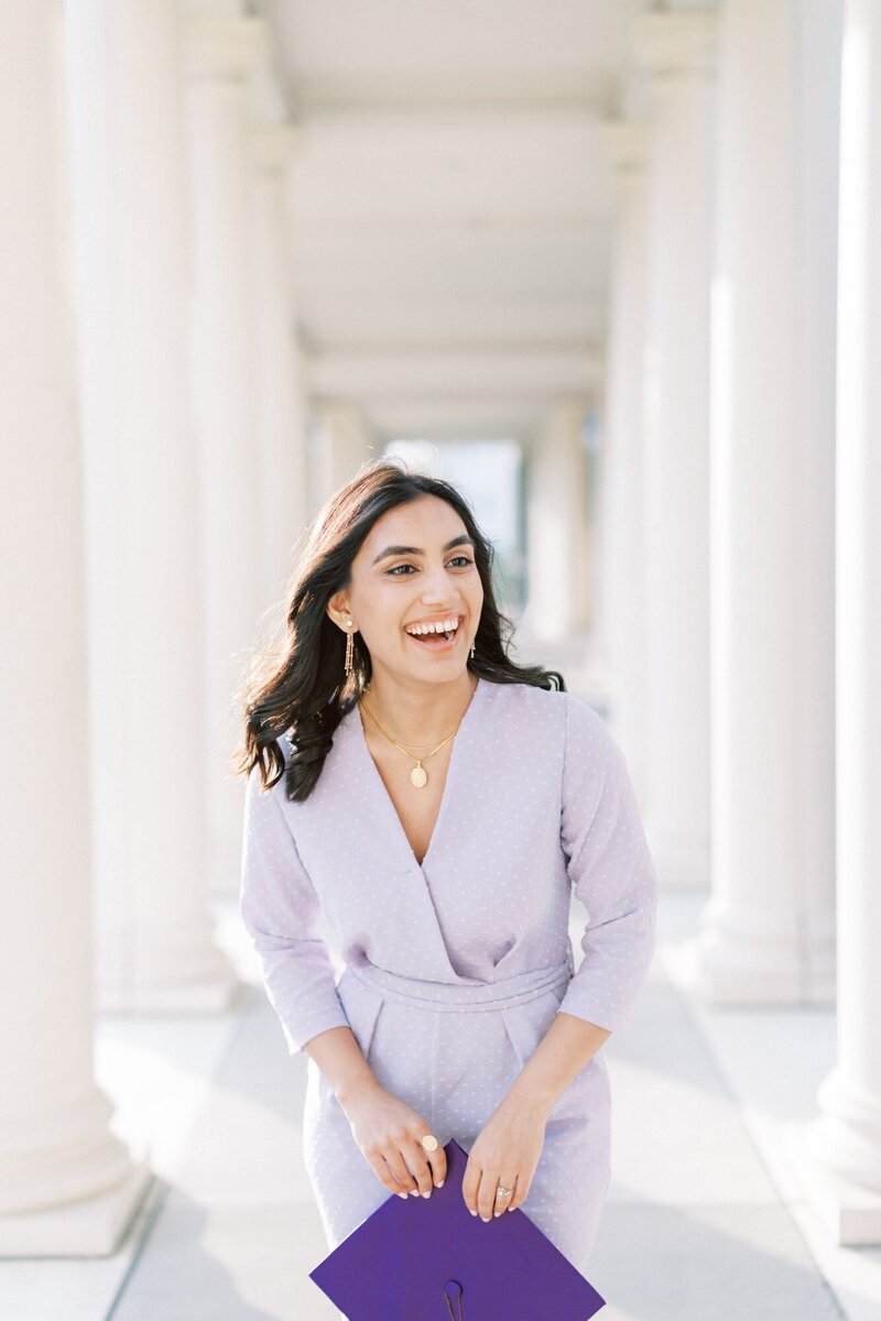An Indian, college graduate girl with  a purple jumpsuit laughs as she is having fun at her senior session at James Madison University in Harrisonburg.