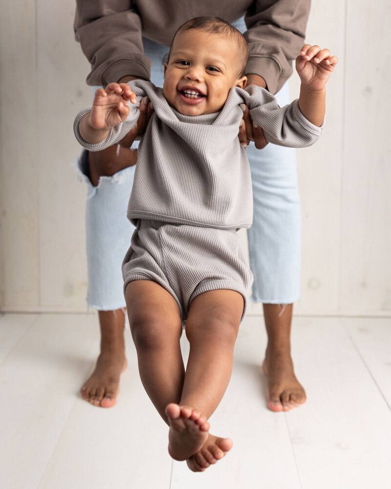 one year old baby swings from his moms hands during his first birthday pictures in Murrysvilole studio.