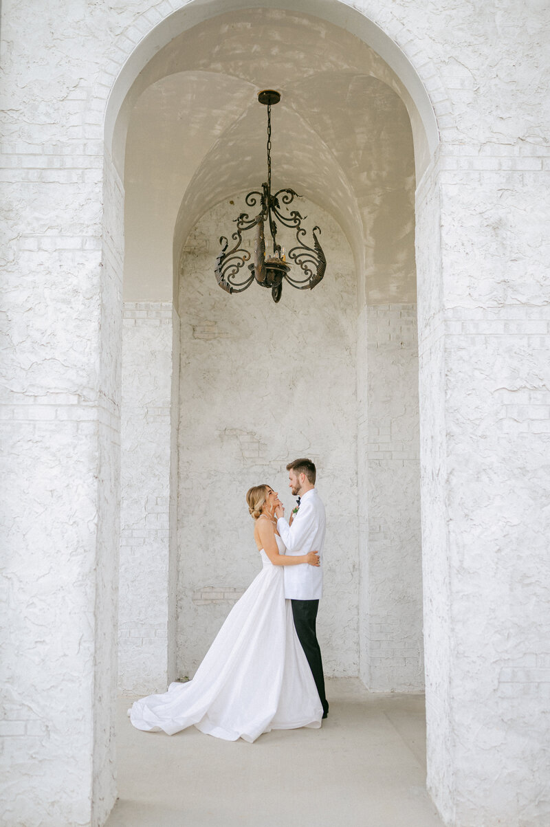 Bride and Groom embrace in a white hall at their wedding venue.
