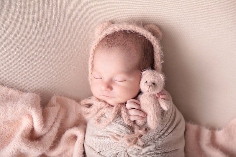 Newborn wrapped in dusty pink swaddle with teddy bear