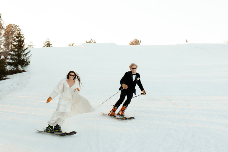 a bride and groom skiing down a hill in wedding attire photographed by claire neville photography