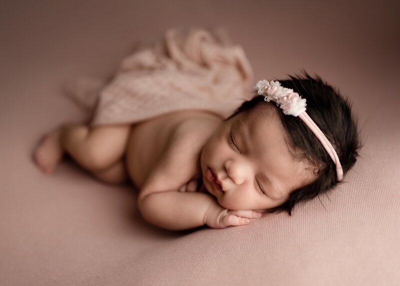Baby portrait. Baby sleeping on belly draped in blush muslin cloth. Baby's hand is under her cheek.