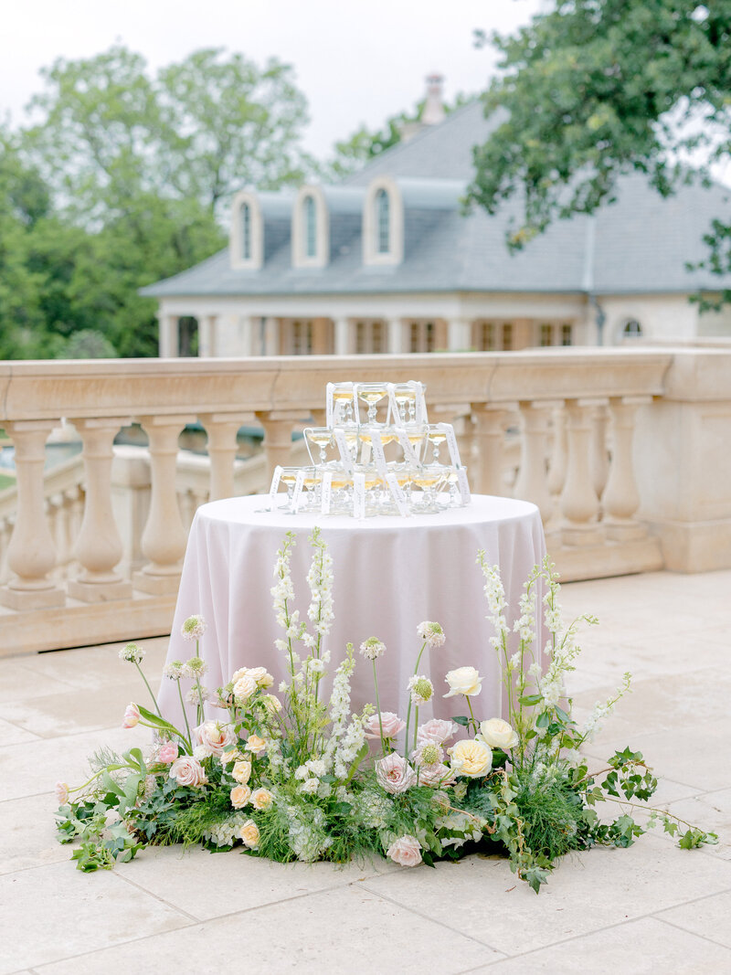 Outdoor table with champagne tower and name cards decorated with greenery and florals on the ground
