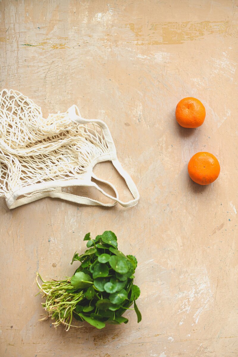 Herbs, oranges, and a netted bag lying on a tan surface