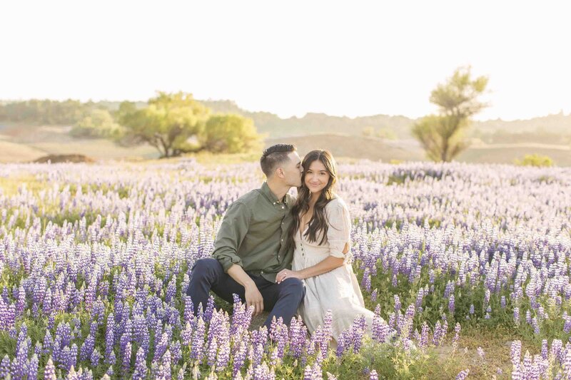 man kissing woman on cheek sitting in lilac field