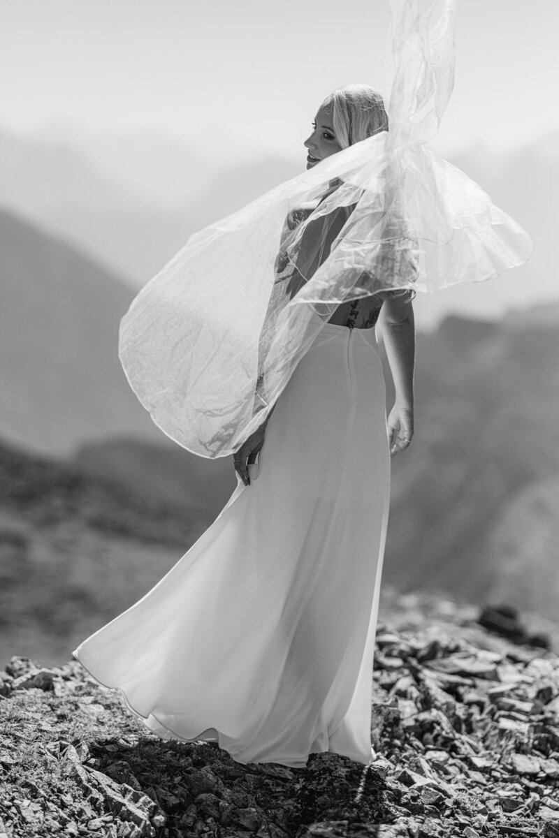 This breathtaking portrait captures a bride standing on a mountain summit surrounded by the majestic Banff mountains after her helicopter wedding. The stunning alpine landscape frames her elegance and joy, celebrating the adventurous and unforgettable moment of her wedding day.