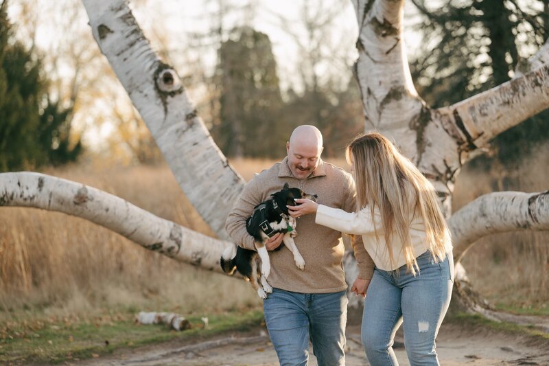 a couple with their puppy at an engagement session by a white birch tree with a Grand Rapids engagement photographer