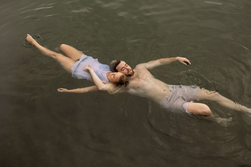 couple floating in water , eyes closed and tenderly holding onto each other 