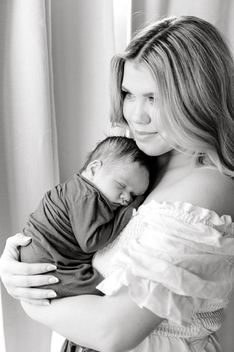 Black and white image of a newborn sleeping on his mom's chest while she holds him