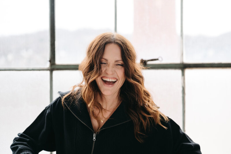 Woman laughing in a room with big windows, embodying the spirit of photography mentoring.