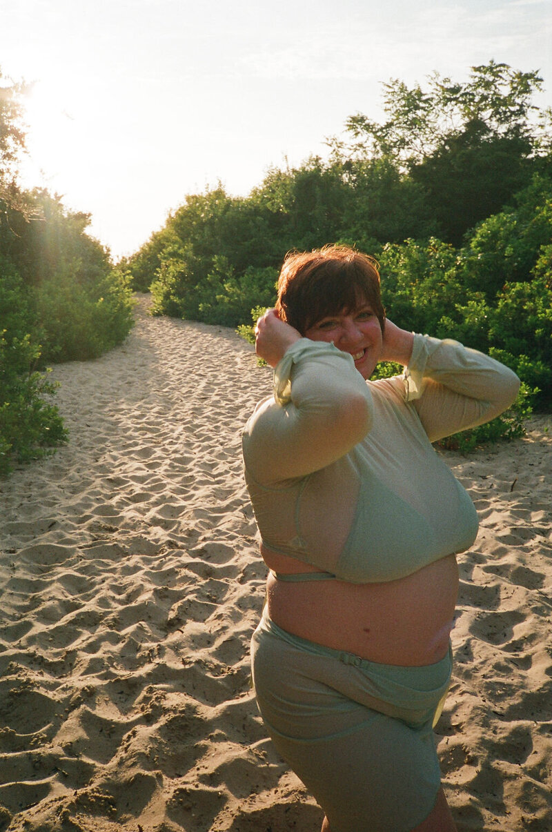 Annie (the artist), looking over her freckled shoulder with a green bodysuit and sheer floral lace robe.