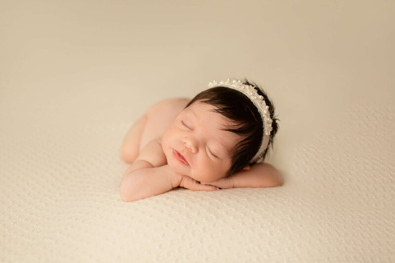Newborn baby boy in a blue swaddle in a tan basket on a tan background