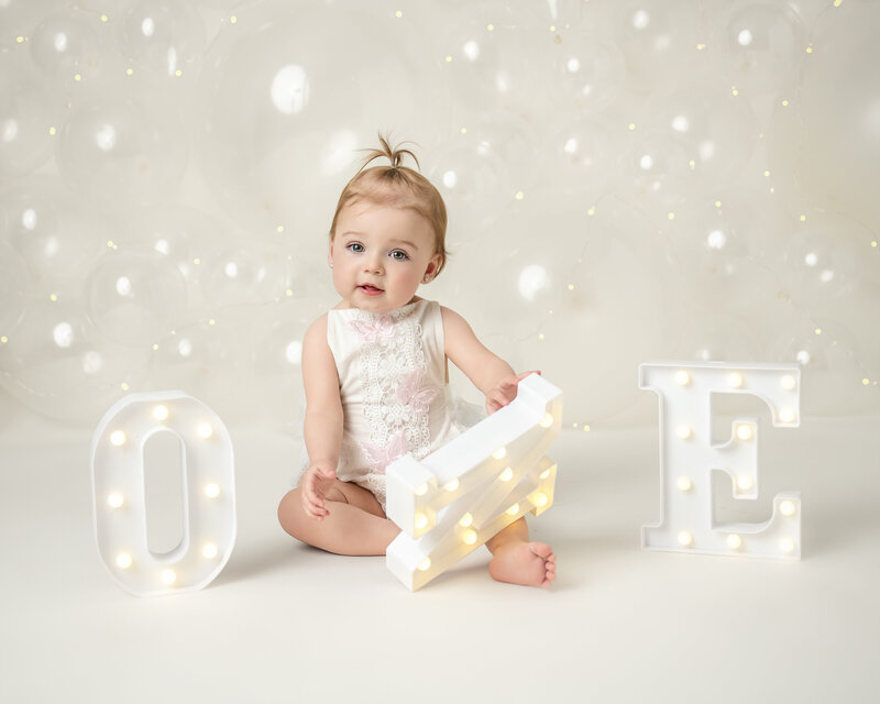 1 year old baby girl sitting with light up letters that spell one