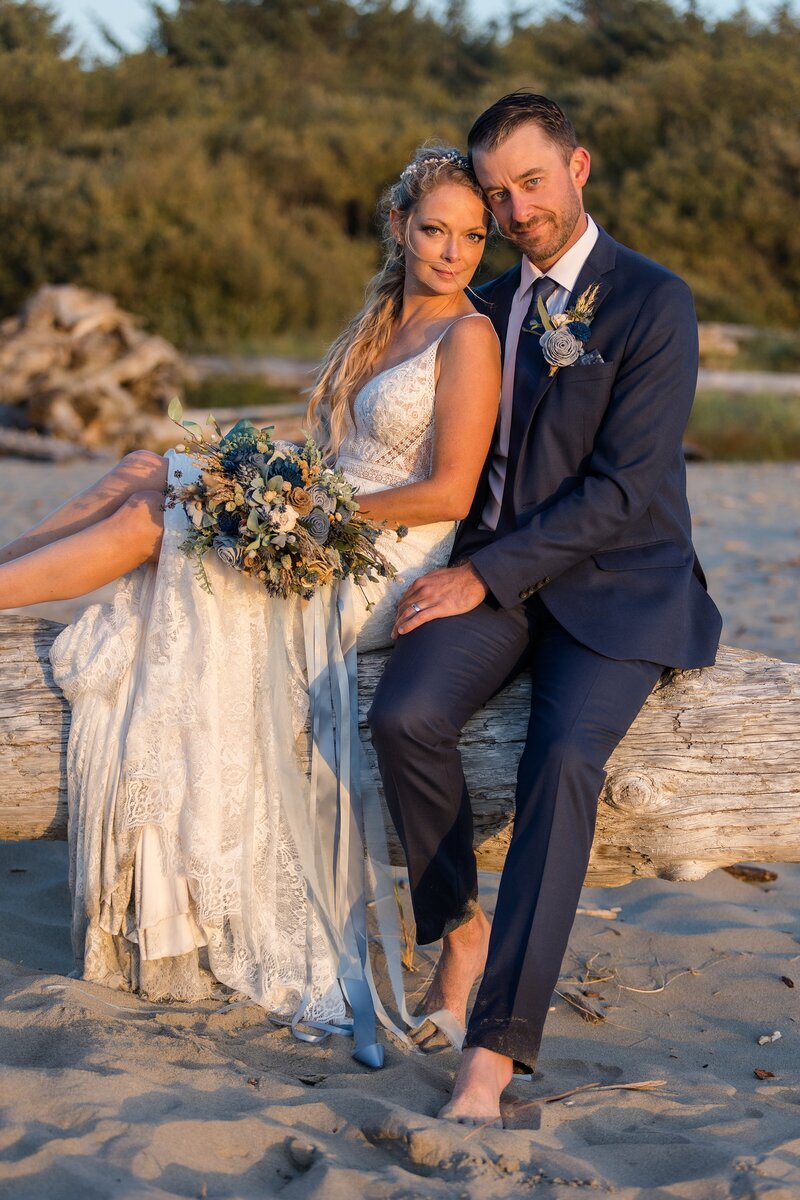 newly married couple sitting on driftwood on the beach