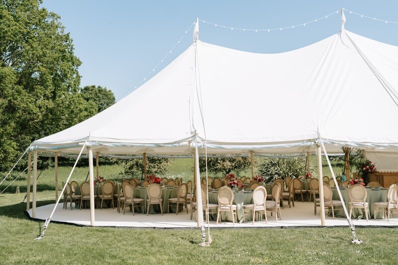A large pole marquee set up on beautiful grounds on the other side of a lake