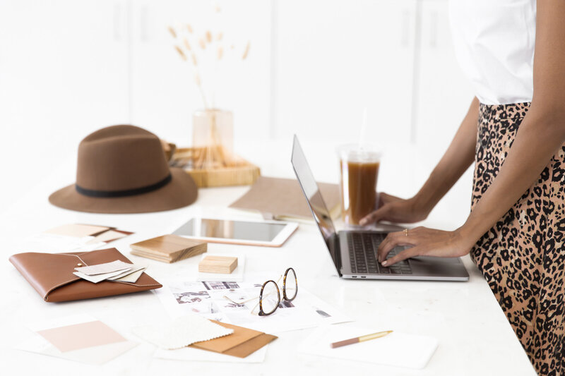 view of desk with office items and woman's hands seen typing on laoptop
