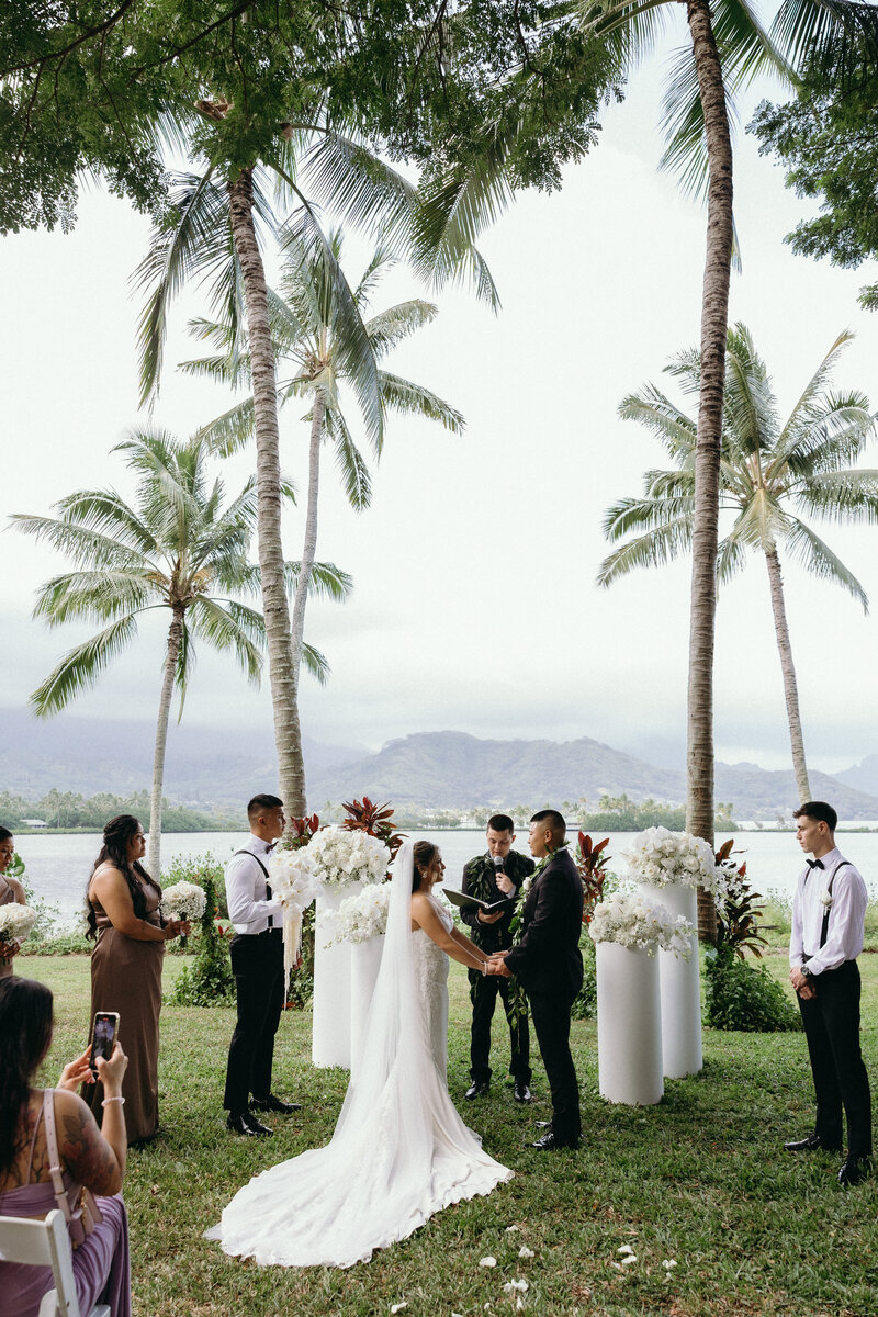 Bride and groom walking hand in hand at Kualoa Ranch with mountain views in the background
