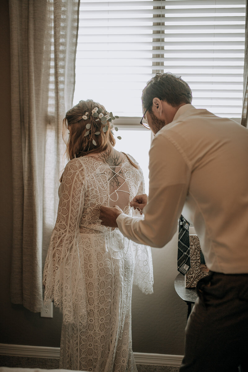 brother helping bride lace up her boho wedding dress