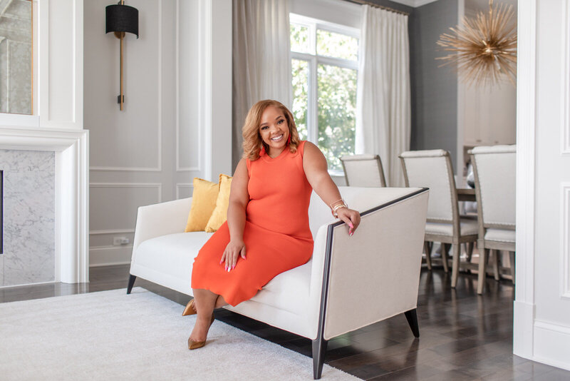 smiling african american woman in orange dress sits on a white couch