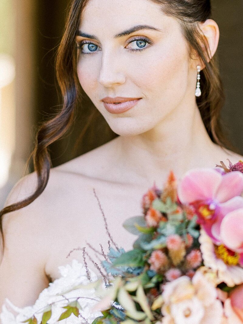 a bride holding a bouquet of beautiful pink flowers with stunning blue eyes during her luxury wedding in Southern California