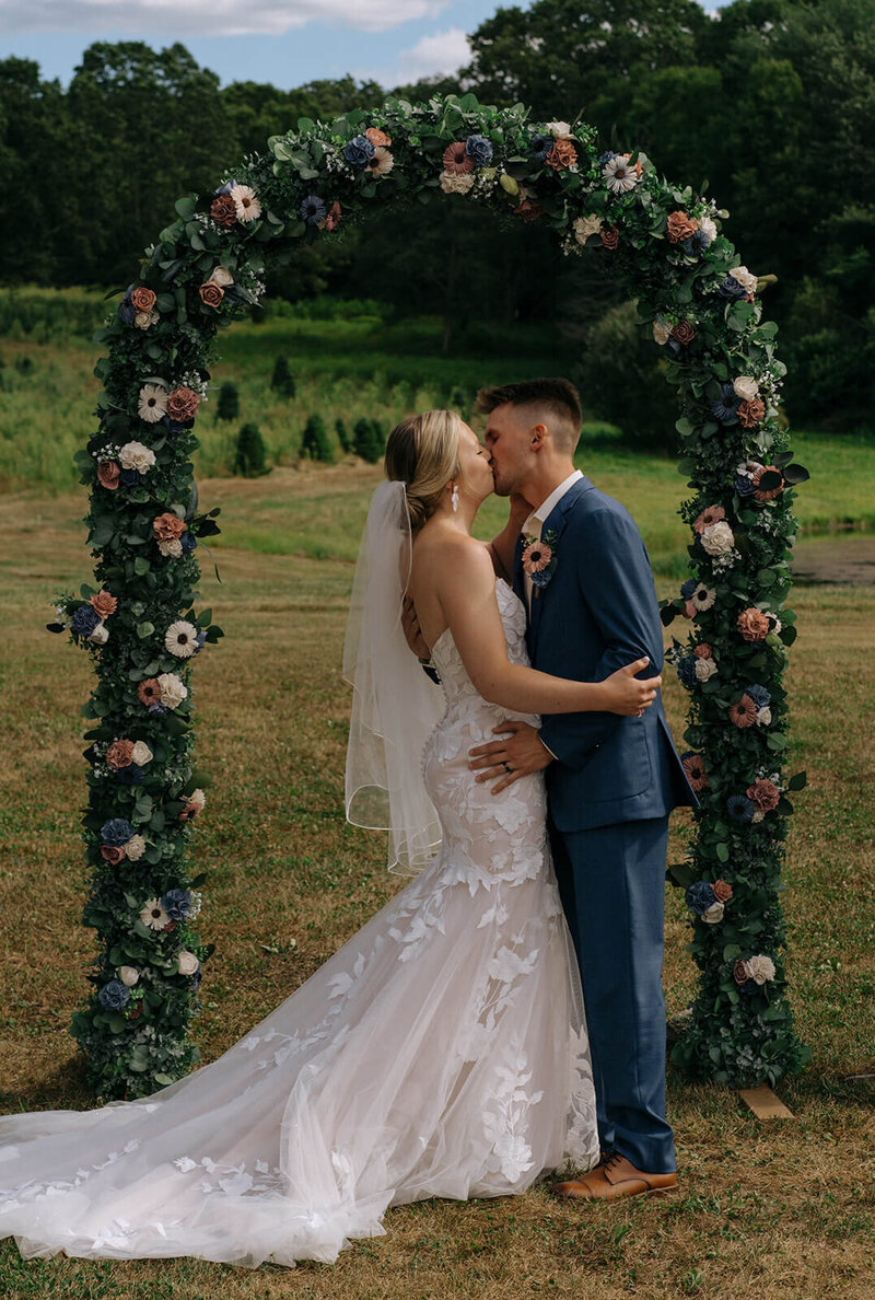 The bride and groom are kissing while standing near the altar during the wedding ceremony in the garden.