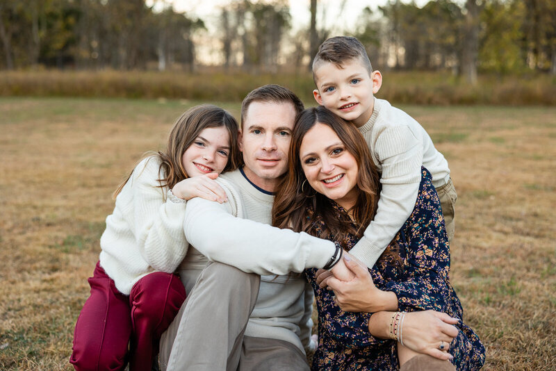 Outdoor family portrait of parents and children sitting on the grass hugging and looking at the camera in Farmington, Missouri. 