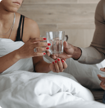 A man passing a woman in bed a glass of water for her vitamins