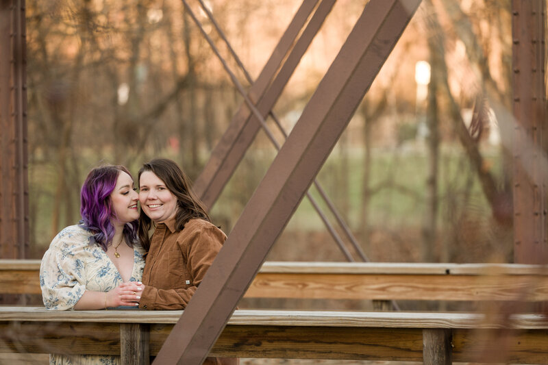 Same-sex couple standing closely on the Iron Bridge in Phoenixville, celebrating their love during their engagement session.