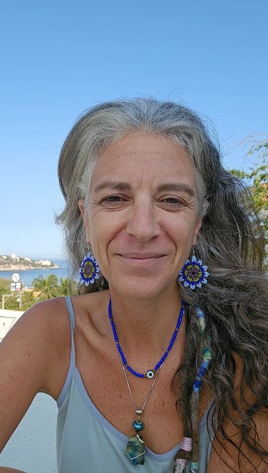 Giovanna Rose, a wellness guide focused on nutrition and healthy living in Puerto Escondido, smiles gently in a coastal outdoor setting. Surrounded by ocean views and nature, she wears vibrant handmade jewelry and radiates a grounded, nourishing energy, reflecting her holistic approach to mindful eating and natural health.