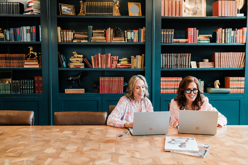 Two professional wedding planners collaborate on laptops at a table, representing Socially Significant Events’ dedication to meticulous event planning and design.