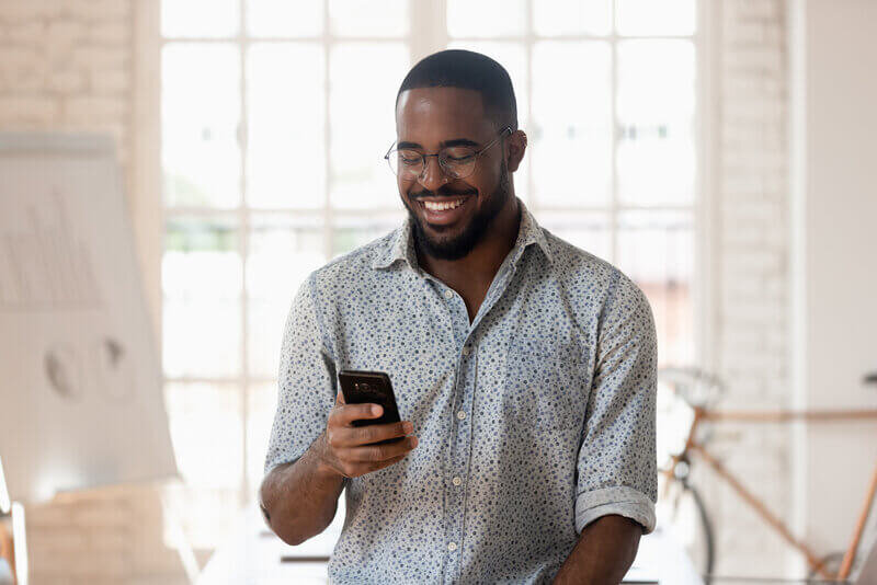 Man with glasses holding phone and laughing at phone