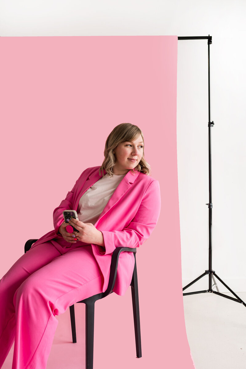 Kat Murphy in a pink blazer sitting in a chair holding her iphone