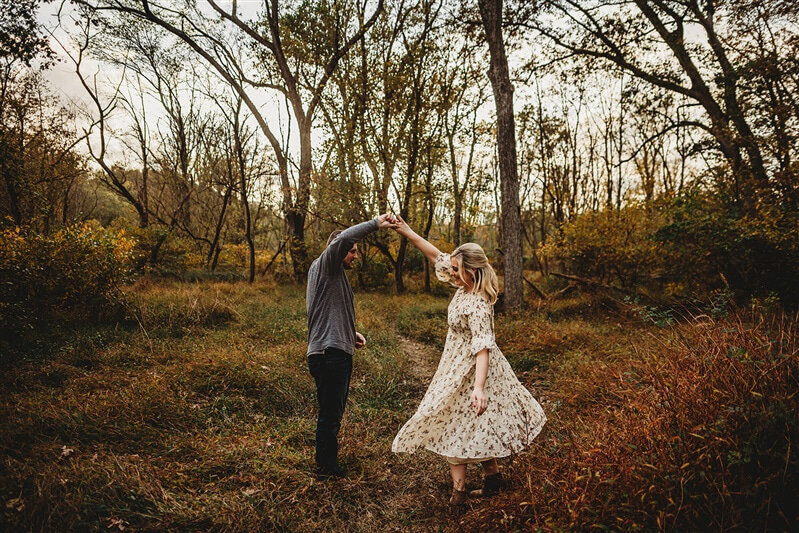 Outdoor couples photography with man twirling woman as they dance together in a field for fall portraits with Baltimore photographer