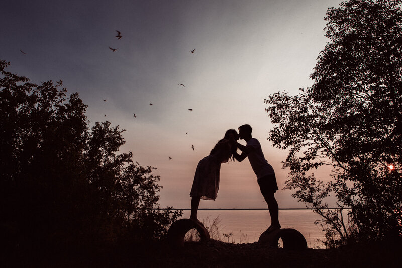 silhouette of couple leaning in and kissing with trees and birds